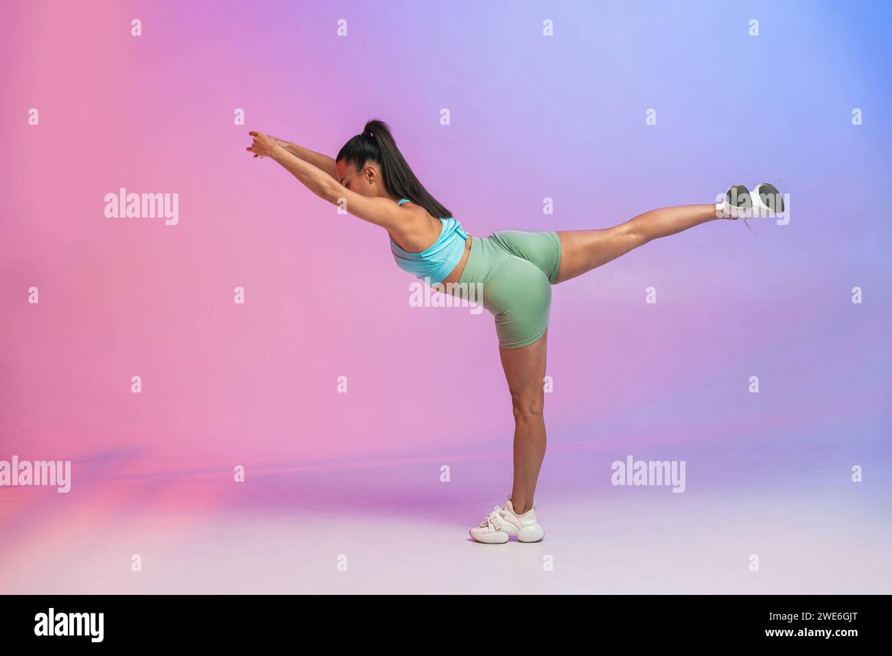 Junge Frau, die auf einem Bein vor farbigem Hintergrund trainiert Stockfoto