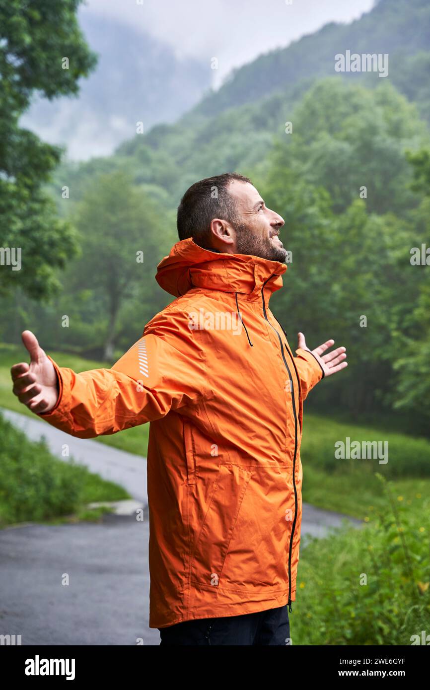 Glücklicher Mann, der orange Jacke vor dem Pyrenäenberg trägt Stockfoto