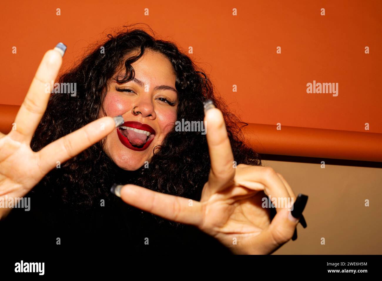 Eine junge Frau, die die Zunge ausstreckt und Friedenszeichen mit Gesten gibt Stockfoto