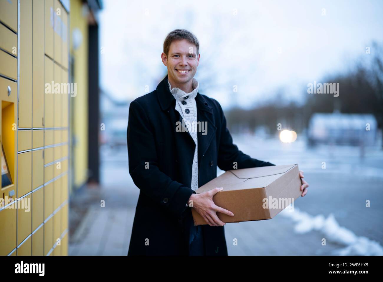 Glücklicher Mann, der mit dem Paketkasten in der Nähe des Paketfachs steht Stockfoto