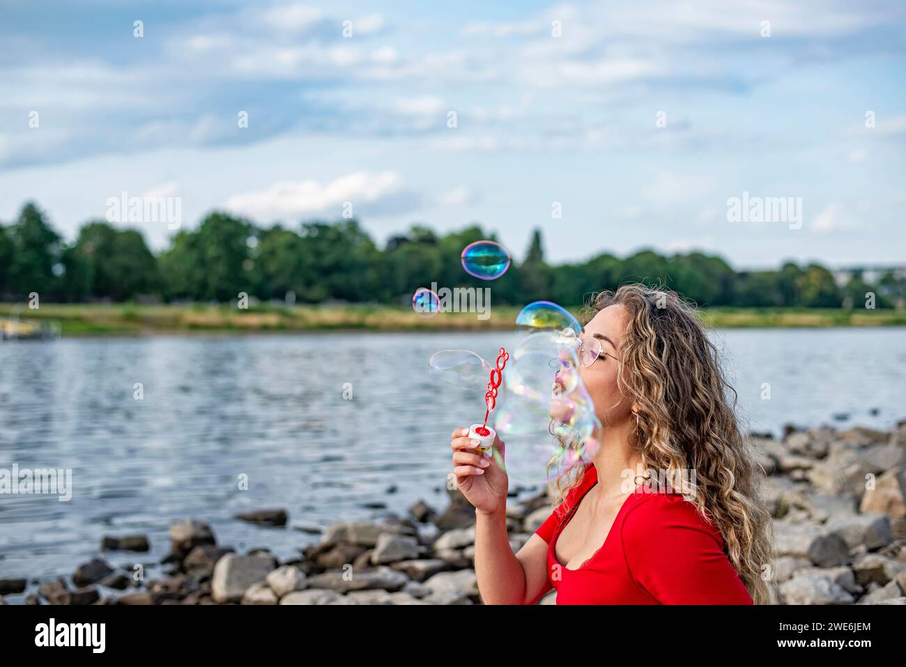 Glückliche junge Frau, die Blasen in der Nähe des Flusses bläst Stockfoto