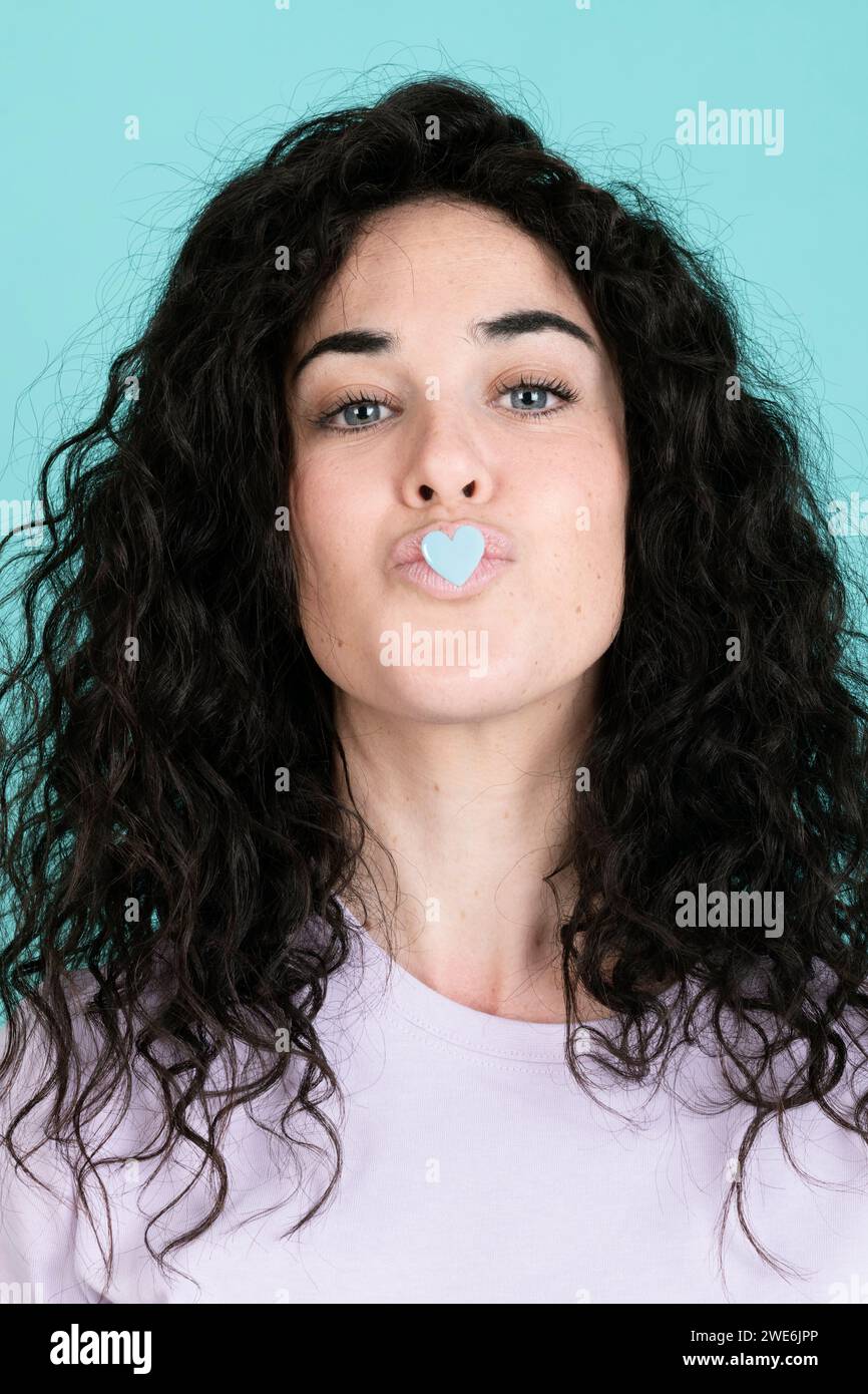 Frau, die mit einem herzförmigen Sticker auf den Lippen vor türkisfarbenem Hintergrund puckt Stockfoto