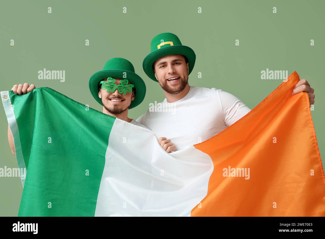 Glückliche junge Männer in Kobold-Hüten mit irischer Flagge auf grünem Hintergrund. St. Patrick's Day-Feier Stockfoto