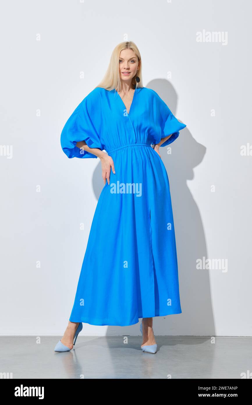 Eine stilvolle Frau mit langen blonden Haaren, die in einem leuchtend blauen Kleid posiert Stockfoto