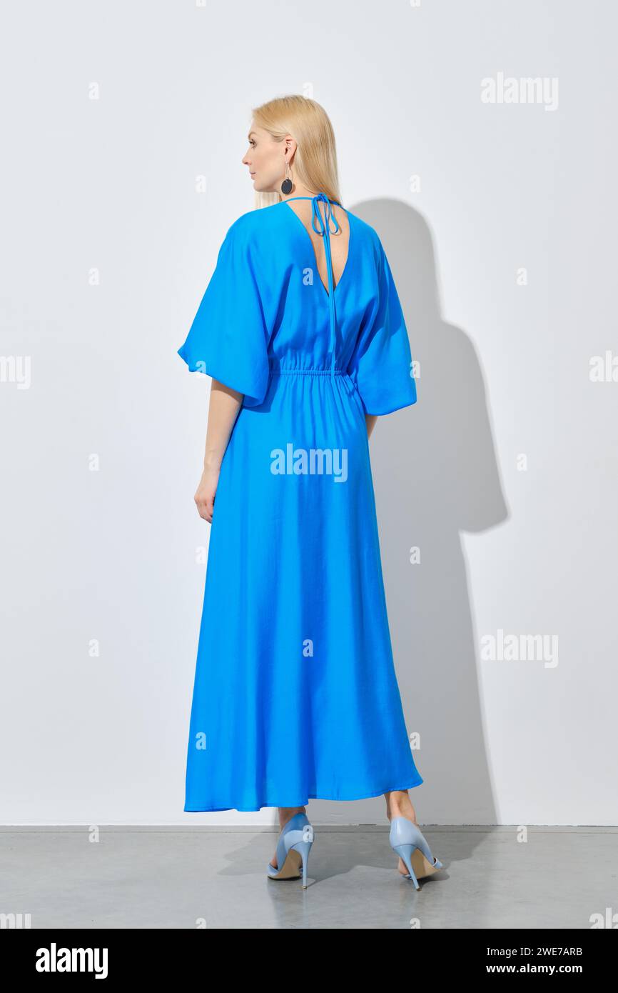 Rückansicht einer blonden Frau in leuchtendem, langem blauem Kleid Stockfoto