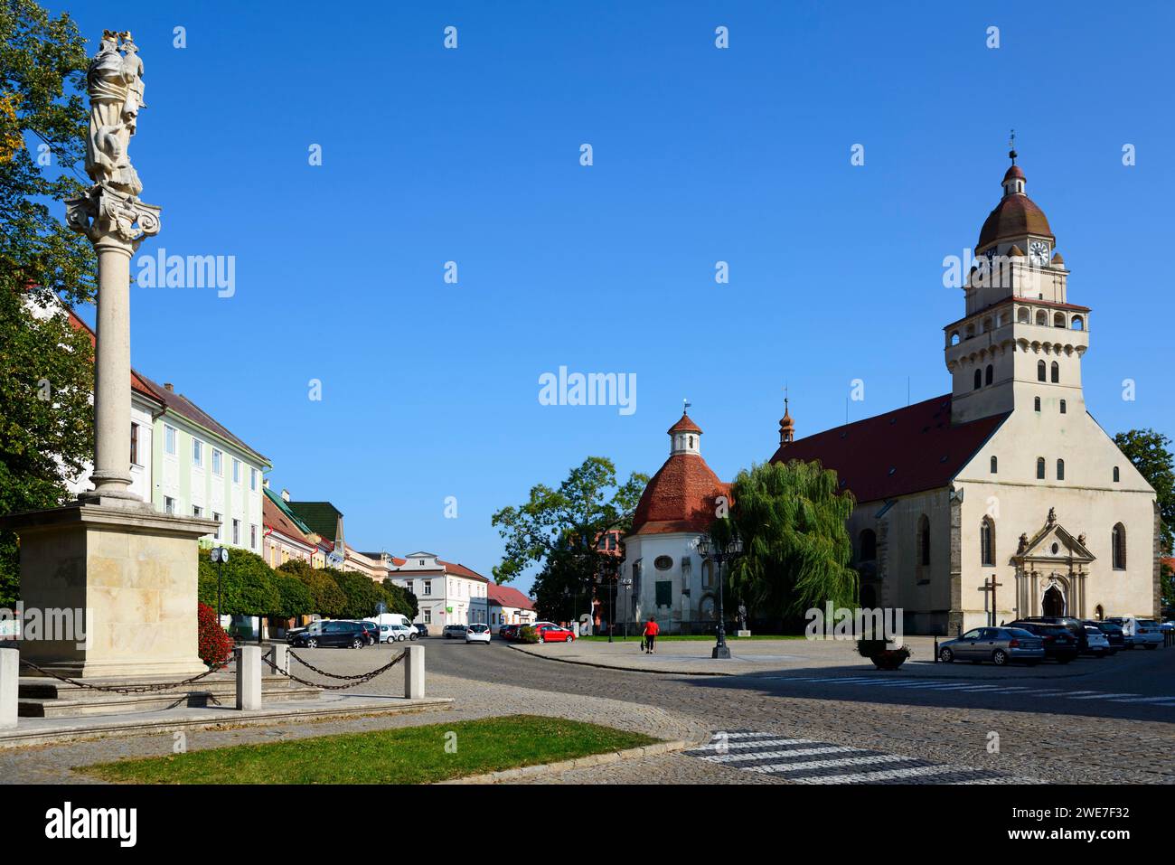 Stadtplatz mit einer Statue im Vordergrund, Kirche im Hintergrund an einem sonnigen Tag, römisch-katholische Pfarrkirche St. Michael, Mariensäule auf Stockfoto