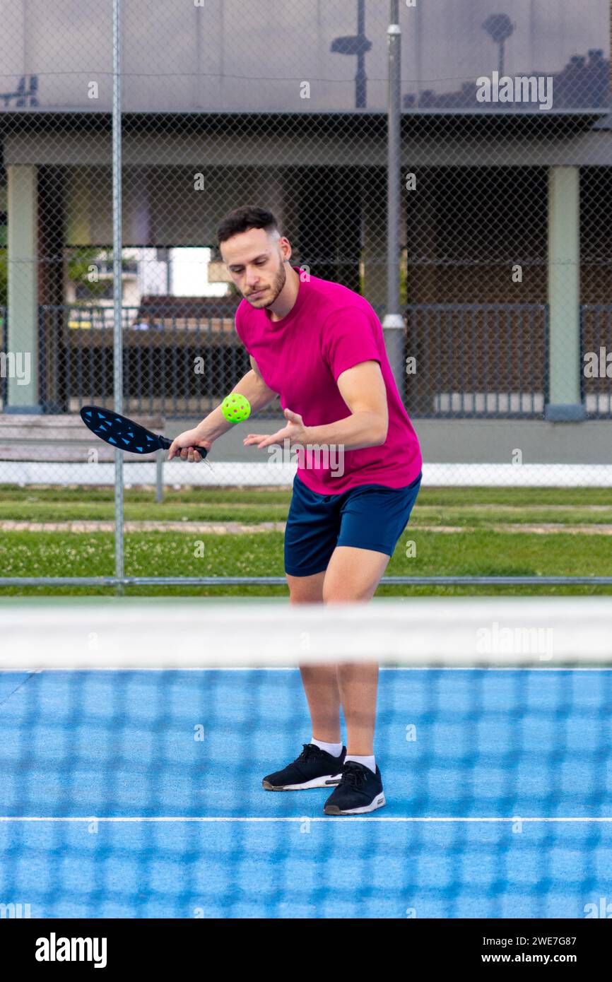 Porträt eines Mannes, der eine Portion im Pickleball vorführt. Sportlicher Spieler mit Pickleball trainiert auf dem Freiplatz mit einem Schläger, um den Ball zu schlagen Stockfoto