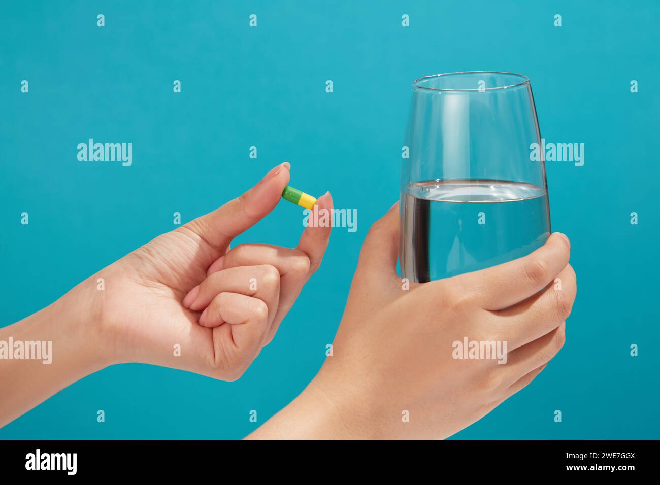 Die minimale Szene einer gelb-grünen Kapsel wird von einem Handmodell gehalten, einem mit Wasser gefüllten Glas in einer anderen Hand. Vitamin kann die Lebensqualität erhöhen Stockfoto