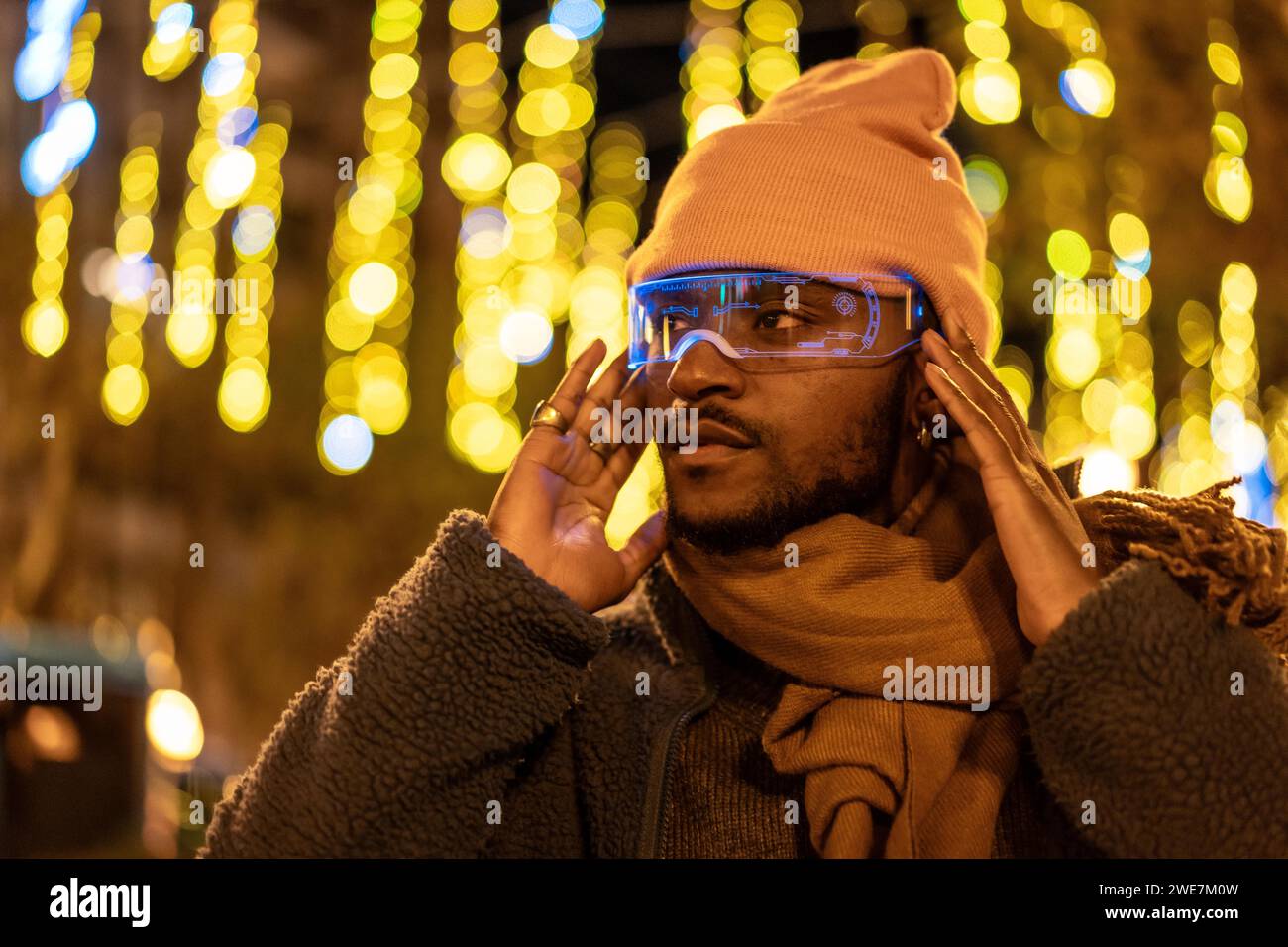 Afrikanischer Mann, der eine intelligente Brille benutzt, in einer futuristischen Stadt mit beleuchteten Straßen bei Nacht Stockfoto