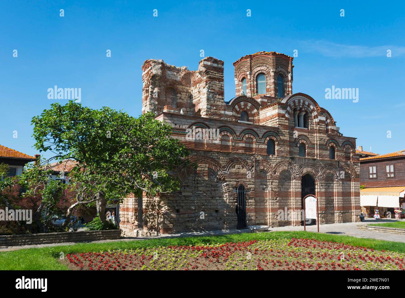 Alte zerbröckelnde Backsteinruinen unter einem klaren blauen Himmel, umgeben von grüner Vegetation und bunten Blumenbeeten, Christ Pantocrator Church, Cross Dome Stockfoto