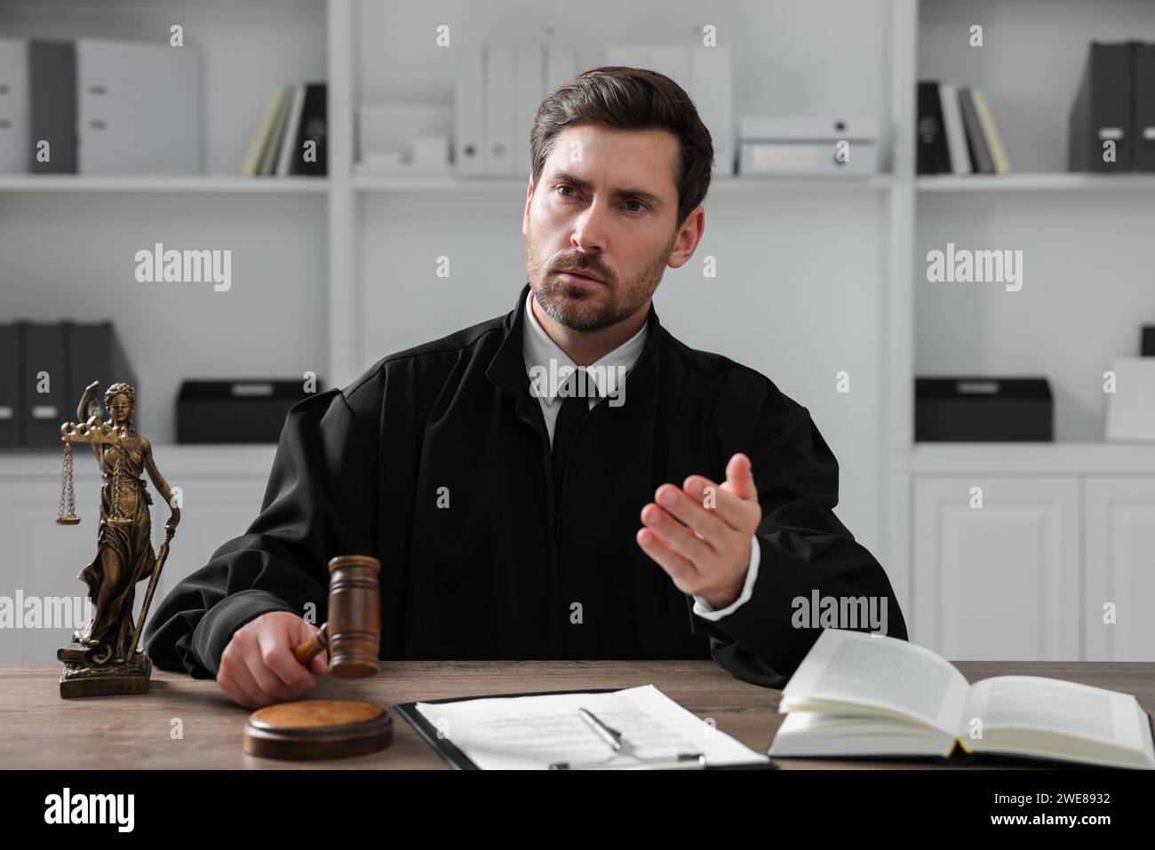 Richter mit Hammer, Papieren und Buch am Holztisch im Büro Stockfoto