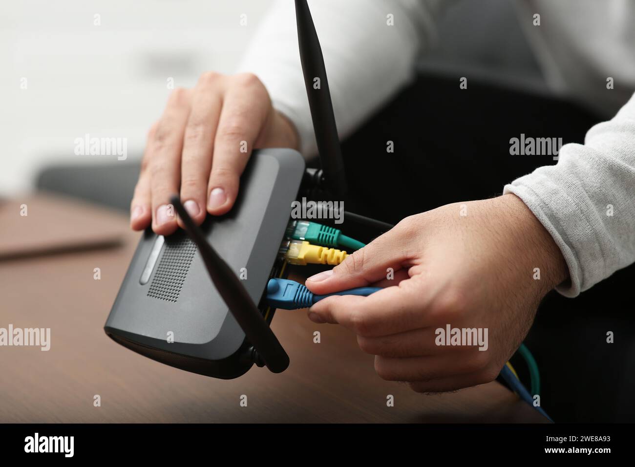 Mann, der Kabel in den WLAN-Router an einem Holztisch drinnen steckt, Nahaufnahme Stockfoto