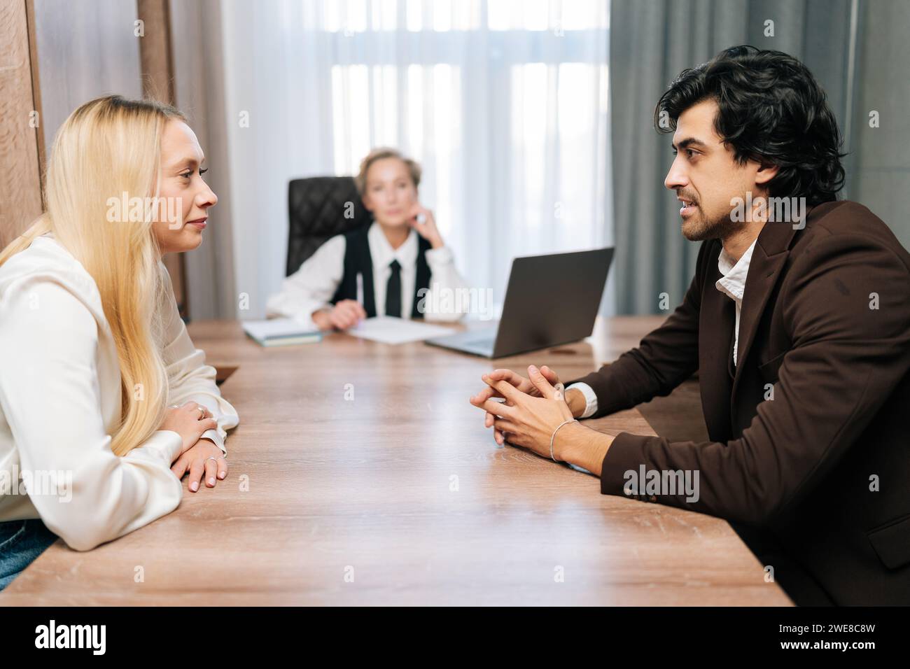 Trauriger junger Mann und Frau, die sich wütend anschauen und sich scheiden lassen, sitzen am Tisch mit Schicht im Büro. Auflösung der Ehe zweier Erwachsener. Stockfoto