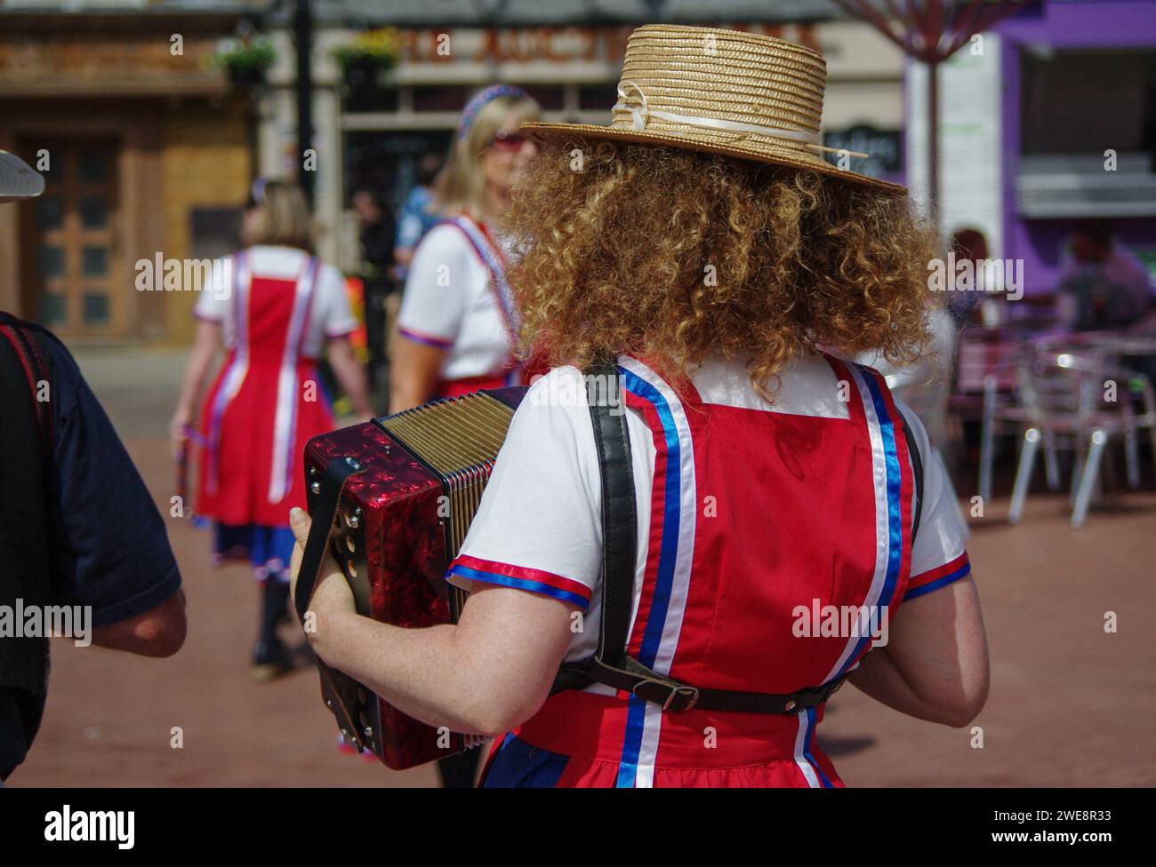 Morris-Tänzer, die auf einer Konferenz auf dem Market Square in Northampton, Großbritannien, eine Ausstellung zeigen; Blick auf eine rothaarige Akkordeonspielerin Stockfoto