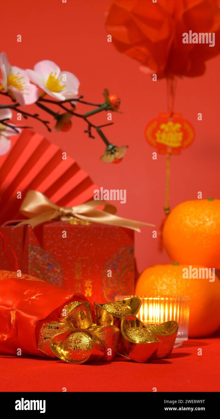 Chinesisches Mondneujahrshintergrund, rotes Thema. Gold im Seidenbeutel, rote Geschenkbox mit goldener Schleife, Papierfächer, Orangen, Pflaumenblütenzweig, Kerze Stockfoto