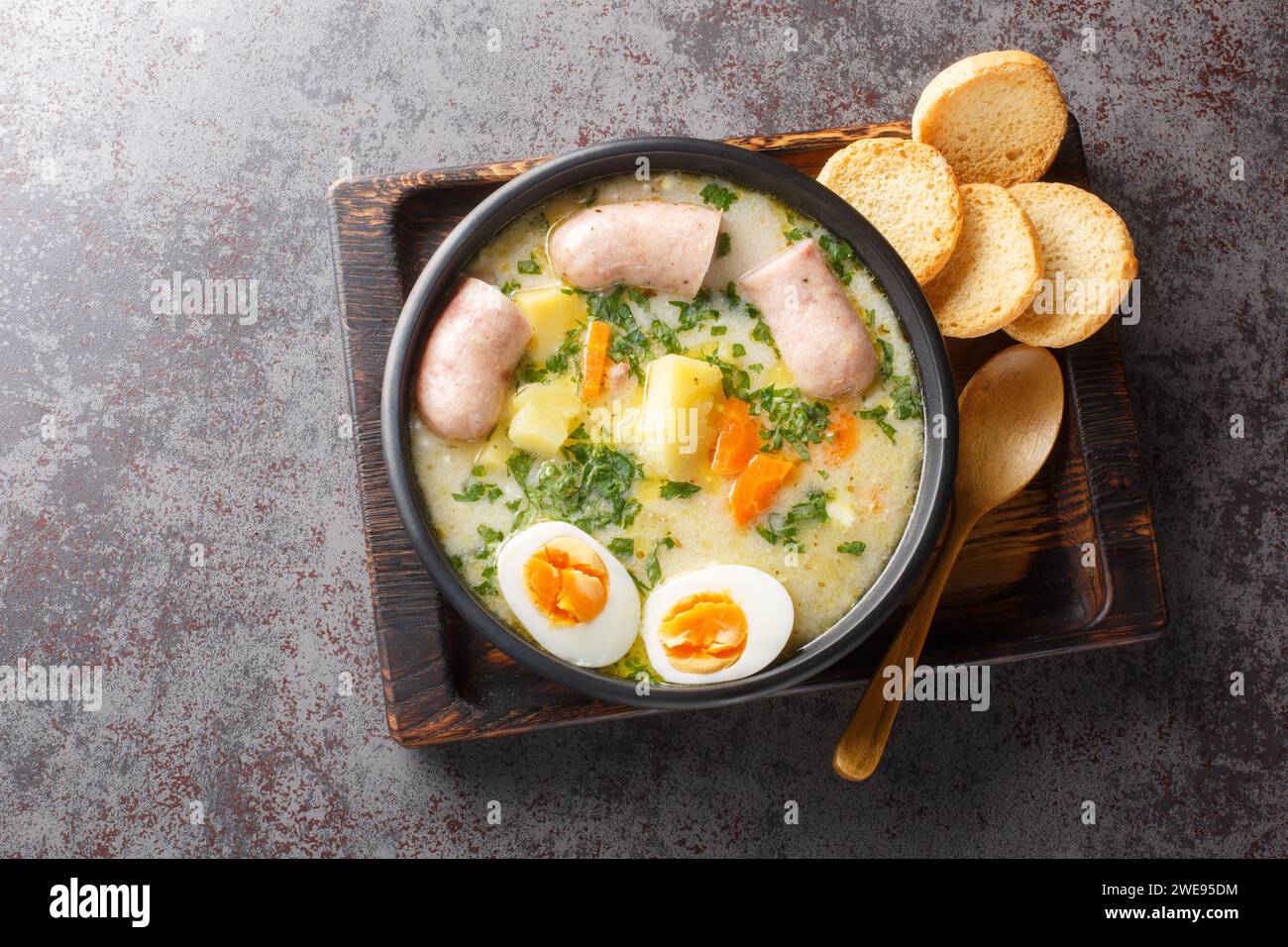 Polnische Roggensuppe Zurek mit Weißwurst, gekochtem Ei und frischem Gemüse in einer Schüssel auf dem Tisch. Horizontale Draufsicht von oben Stockfoto
