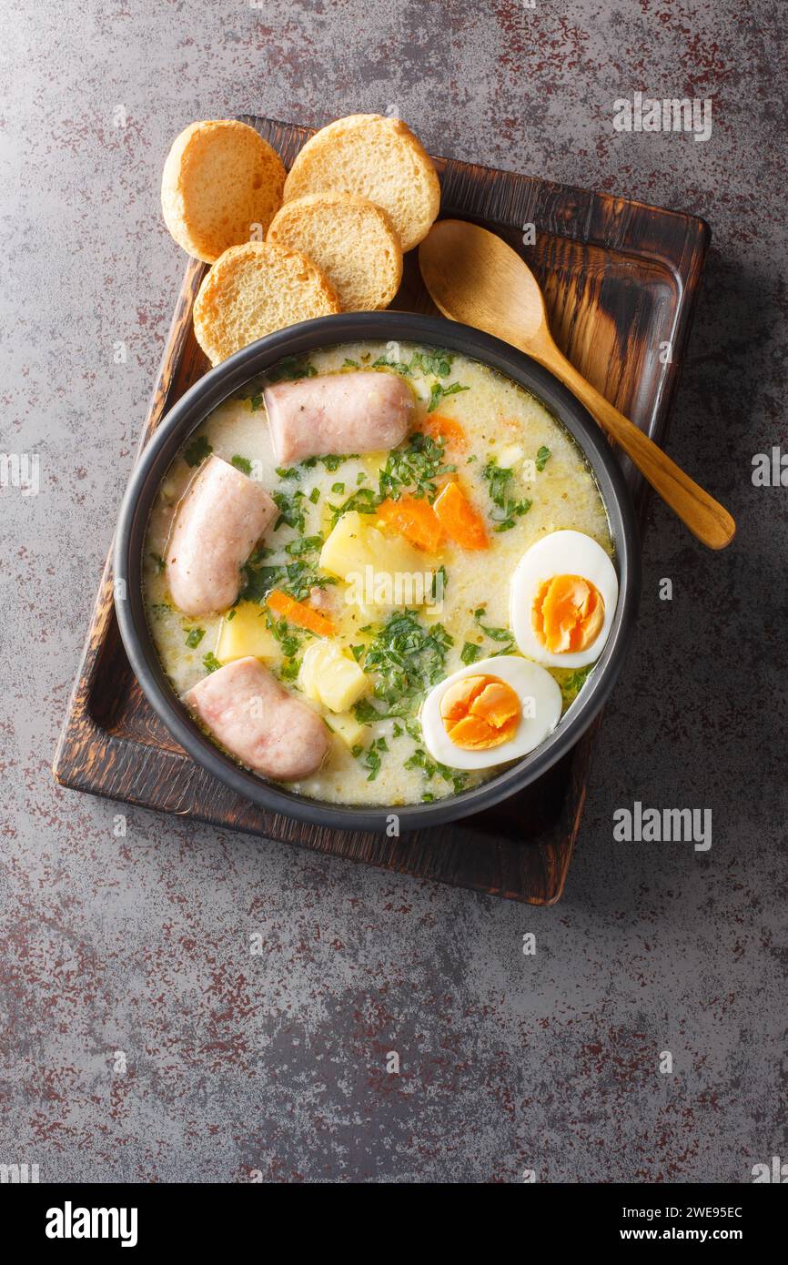 Authentisches zurek eine deftige polnische Roggensuppe mit reichhaltiger weißer Wurst und frischem Gemüse in einer Schüssel auf dem Tisch. Vertikale Draufsicht von oben Stockfoto