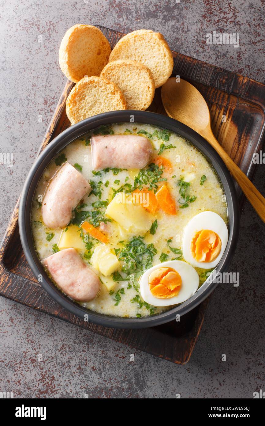 Poliersuppe zurek mit Weißwurst und Eiern in einer Schüssel auf dem Tisch. Vertikale Draufsicht von oben Stockfoto