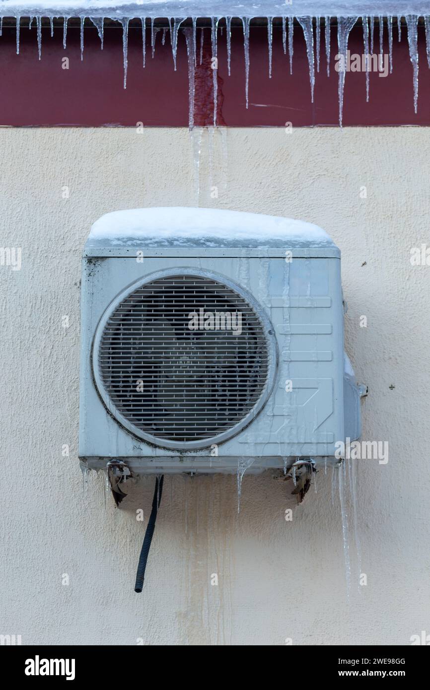 Der Conditioner ist mit Eiszapfen an einer gelben Wand bedeckt. Betrieb der Klimaanlage im Winter bei niedrigen Temperaturen. Kühlung, kalte Konzeptbild. Stockfoto