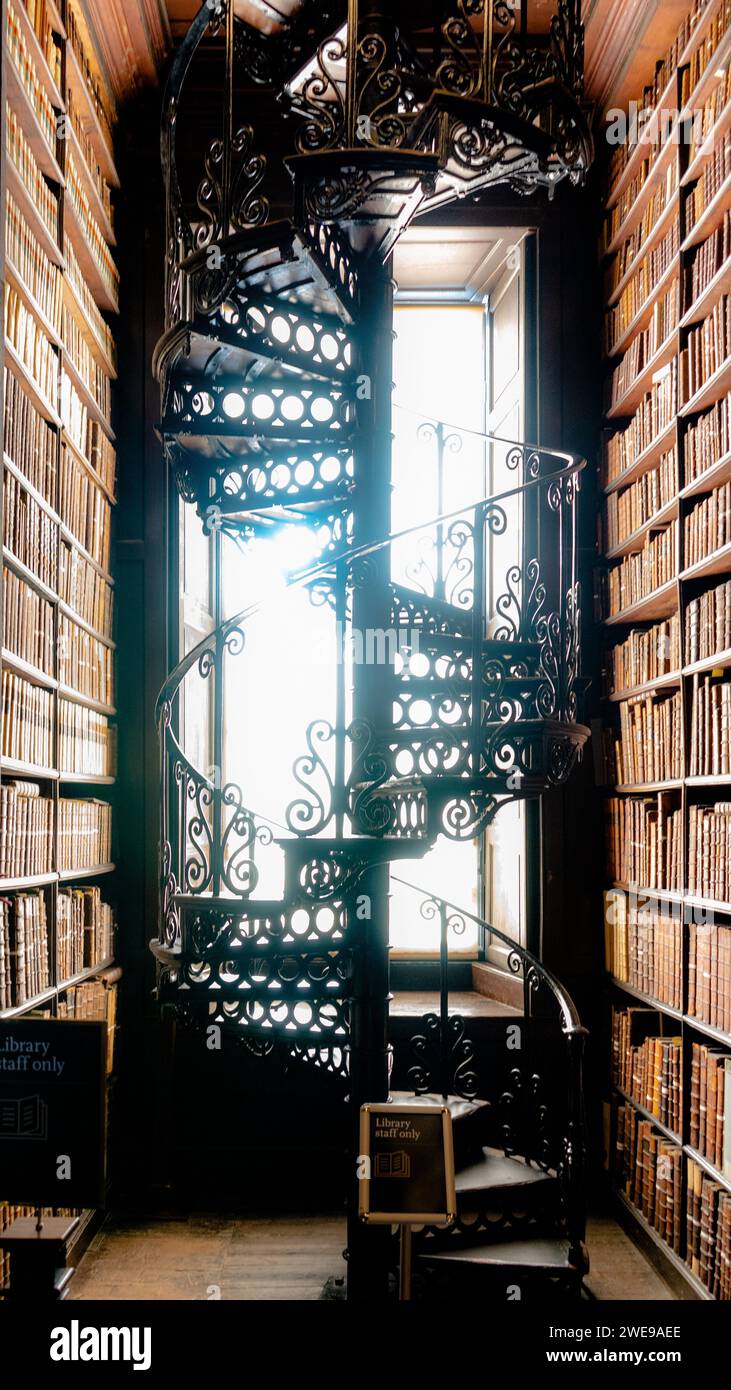 Verzierte, schmiedeeiserne Wendeltreppe in einer klassischen Bibliothek mit raumhohen Bücherregalen. Stockfoto