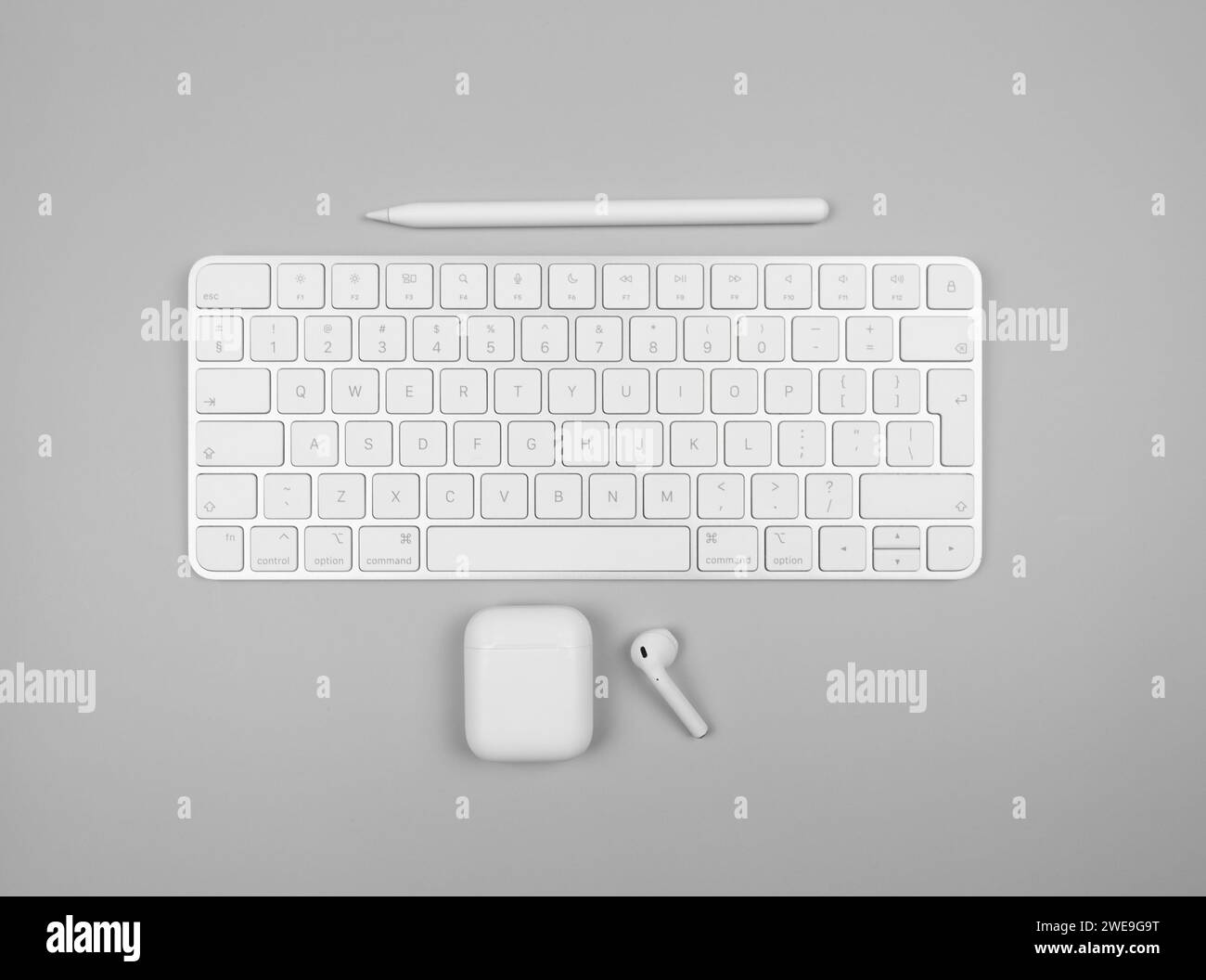 Draufsicht auf weiße Tastatur, Kopfhörertasche und Stift auf hellgrauem Hintergrund. Modernes Büro, Flachbett, Kopierraum. Stockfoto
