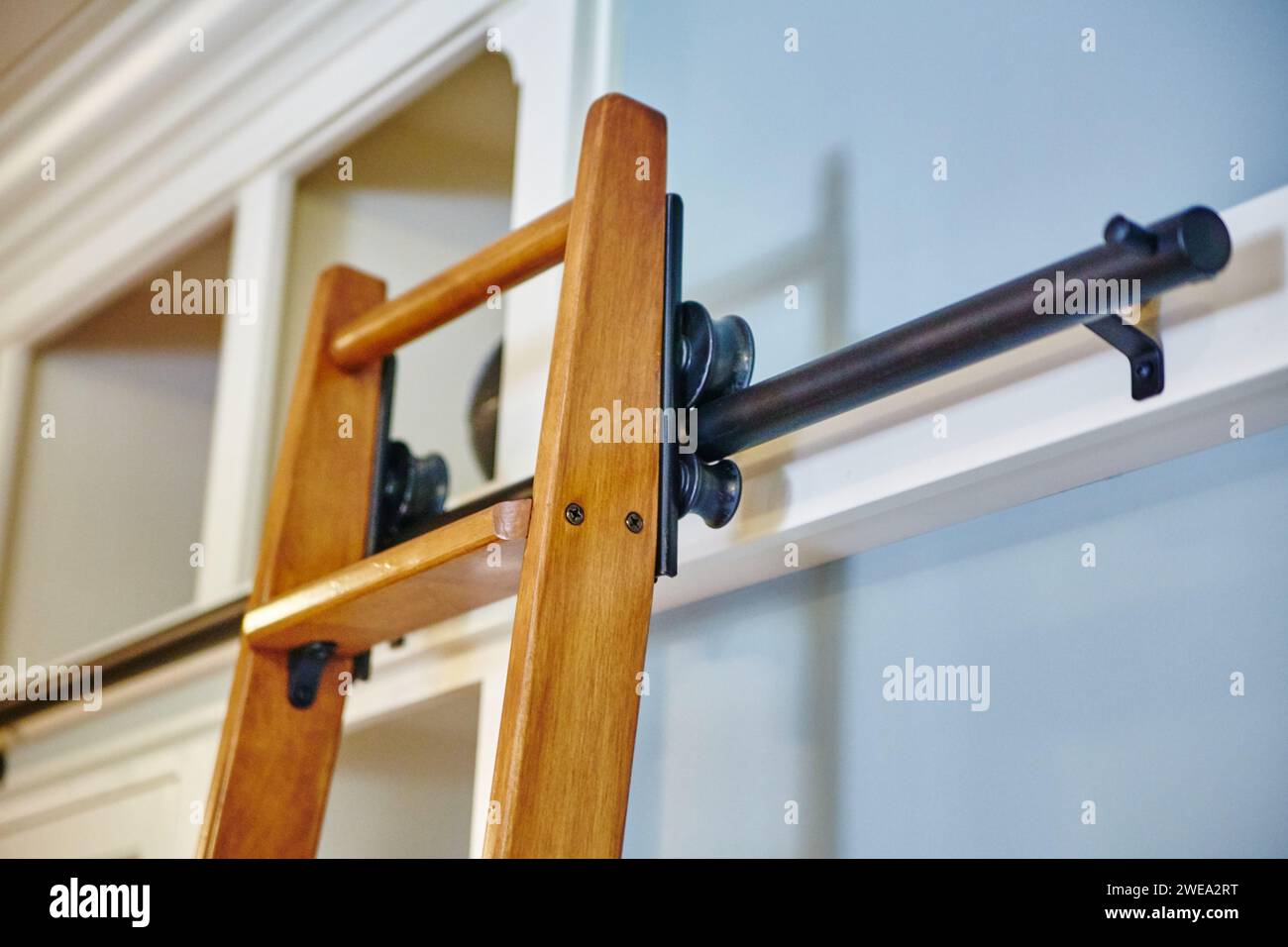 Moderne Holzleiter gegen weiße Wand mit Metallbeschlägen Stockfoto