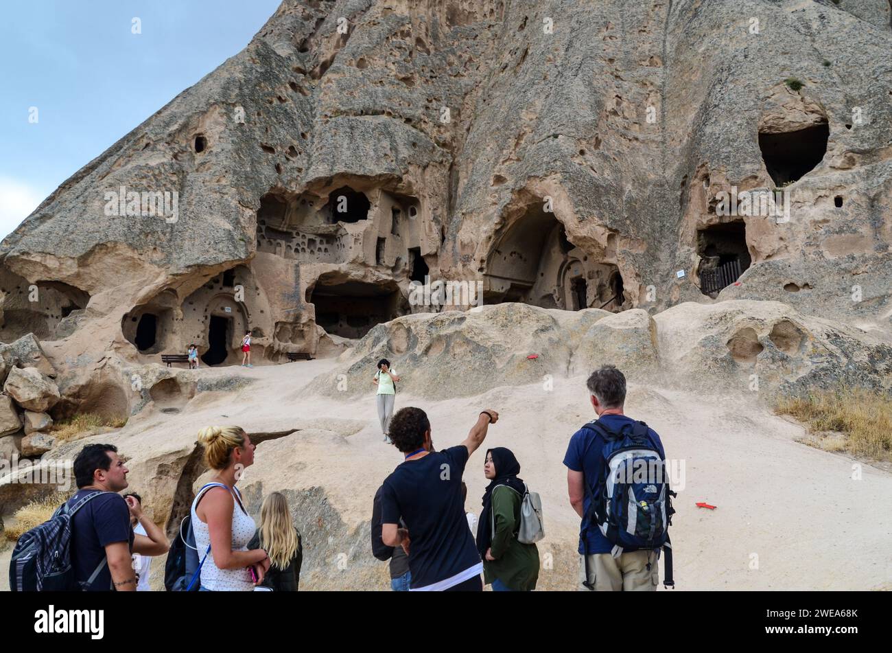Touristen besuchen die alten Höhlenhäuser in einer felsigen Landschaft in Kappadokien, Türkei, mit einem Reiseleiter, der Ihnen Details zeigt. Stockfoto