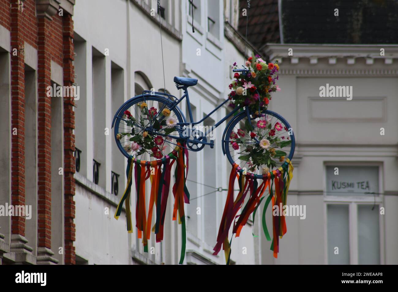 Foto eines hängenden Fahrrads, das in Blumen und Luftschlangen für eine schöne Straßenatmosphäre in Amsterdam gebaut wurde Stockfoto