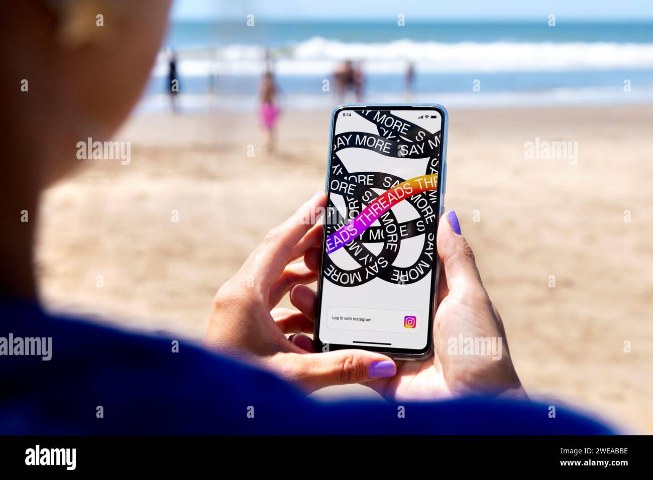 Threads-App wird auf einem Smartphone-Bildschirm geöffnet. Frau am Strand mit einem Handy in der Hand. Textbasierte Konversationsanwendung. Soziales Netzwerk Stockfoto