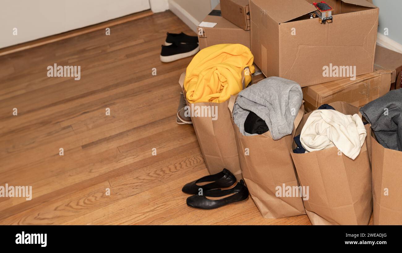 Pappkartons mit Kleidung, Schuhe auf dem Boden Sachen und Sachen zum Umziehen, Umzugstag und Umzugskonzept mit Kopierraum. Stockfoto