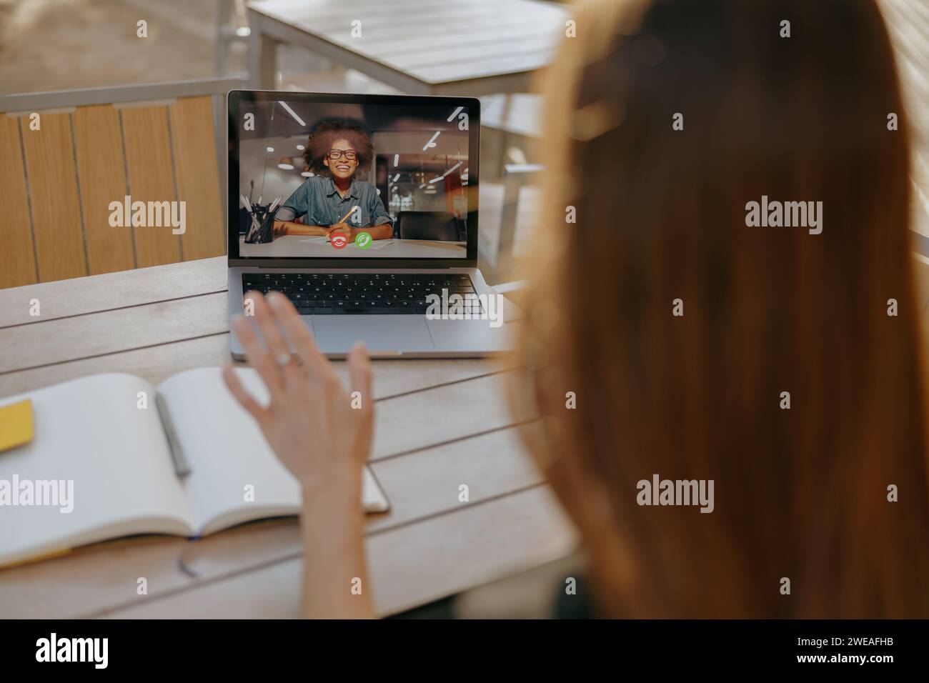 Rückansicht einer Geschäftsfrau, die mit dem Kunden per Videoanruf sprach und Hi winkte, die auf der Terrasse des Cafés sitzt Stockfoto