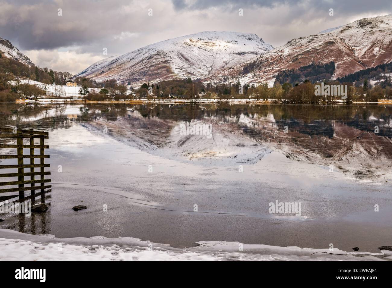 Der Grasmere Lake im Lake District Cumbria UK spiegelt sich vor einem Hintergrund aus schneebedeckten Bergen und eisblauem Wasser wider Stockfoto