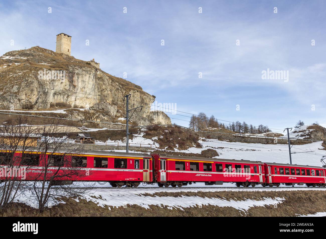 Ardez, Schweiz - 27. Januar 2022: Ruine Steinsberg aus der mittelalterlichen Burg Steinsberg mit einem fahrenden roten Personenzug aus der Rhatia Stockfoto