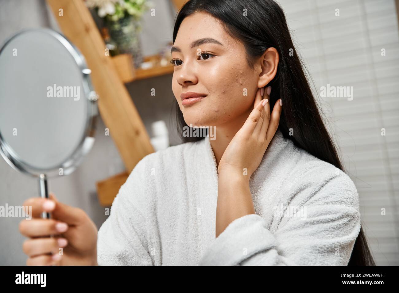 Porträt einer Brünette und jungen asiatischen Frau mit Makeln, die in den Spiegel im modernen Badezimmer blicken Stockfoto