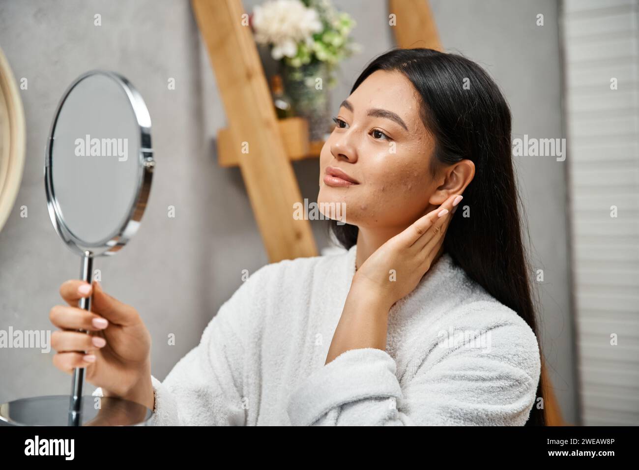 Brünette und junge asiatische Frau mit zu Akne neigender Haut im Spiegel im modernen Badezimmer, Hautpflege Stockfoto