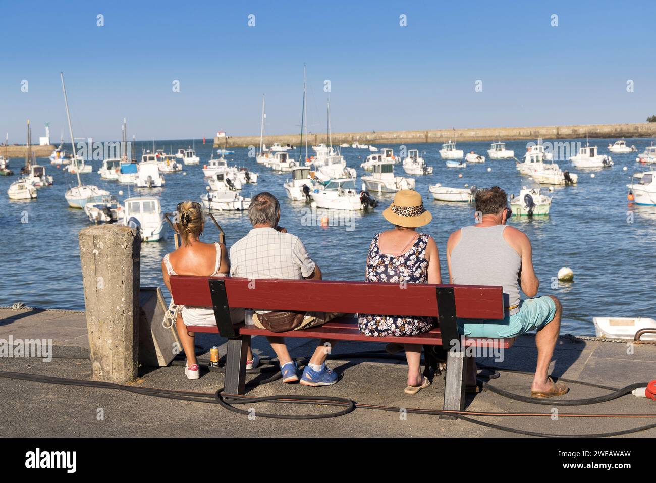 Leute, die sitzen und Boote im Hafen, Barfleur, Manche, Normandie, Frankreich anschauen Stockfoto