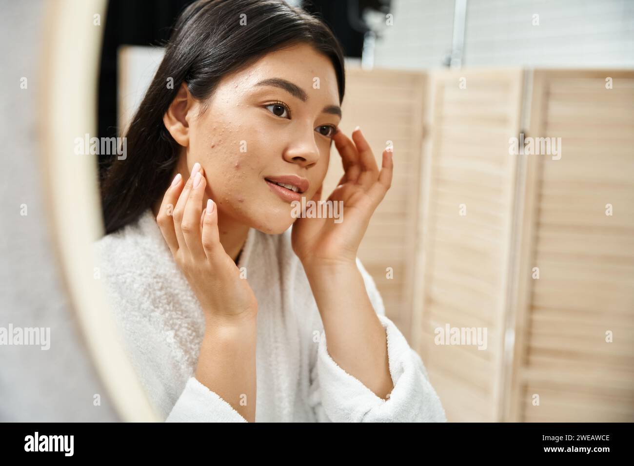 Junge asiatische Frau mit brünetten Haaren, die ihre Haut im Badezimmerspiegel untersucht, Hautzustand Stockfoto