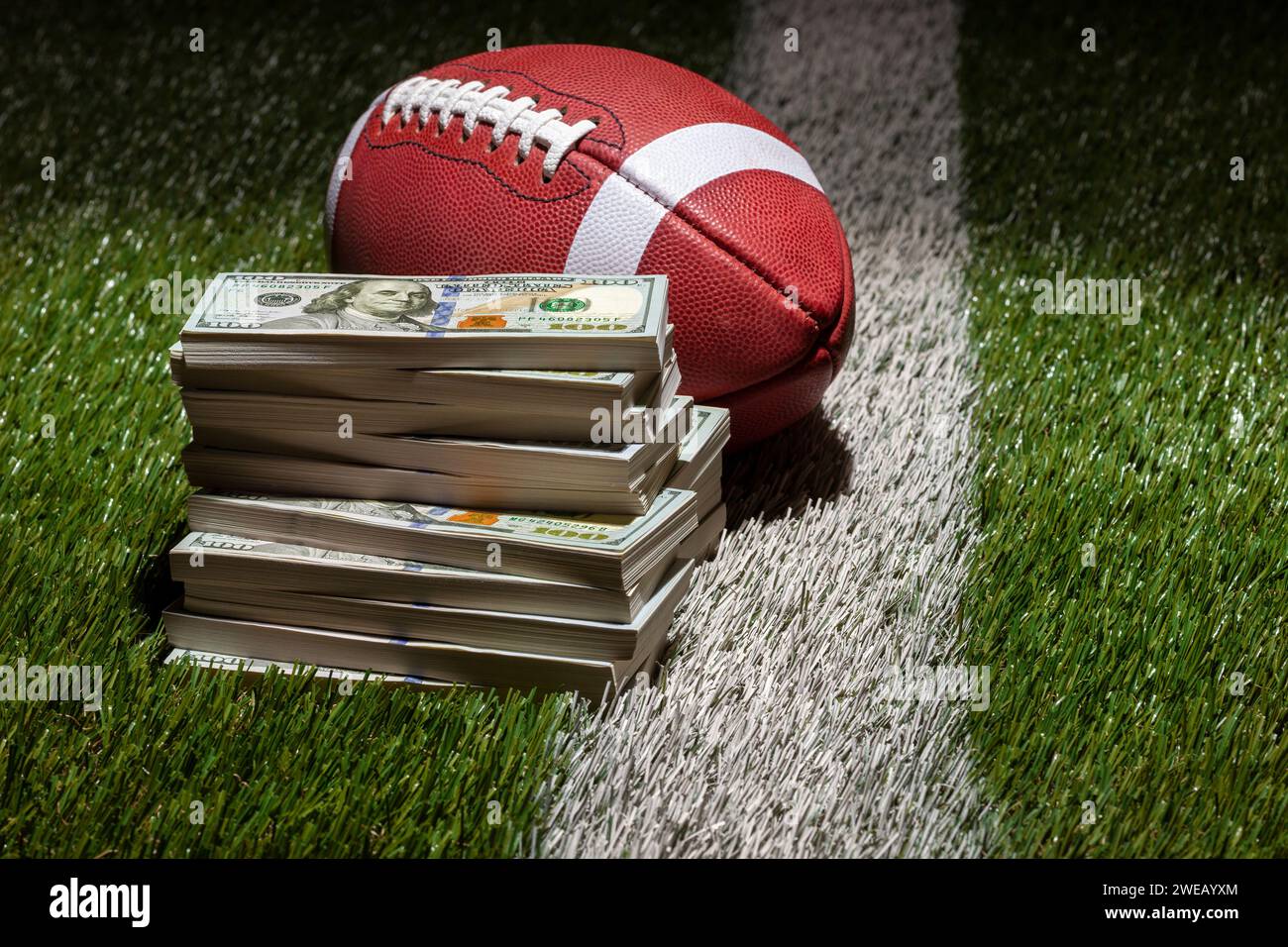 Ein Fußball und ein Haufen von 100 Dollar Scheine auf einem Rasenfeld mit Streifen und dunklem Hintergrund Stockfoto