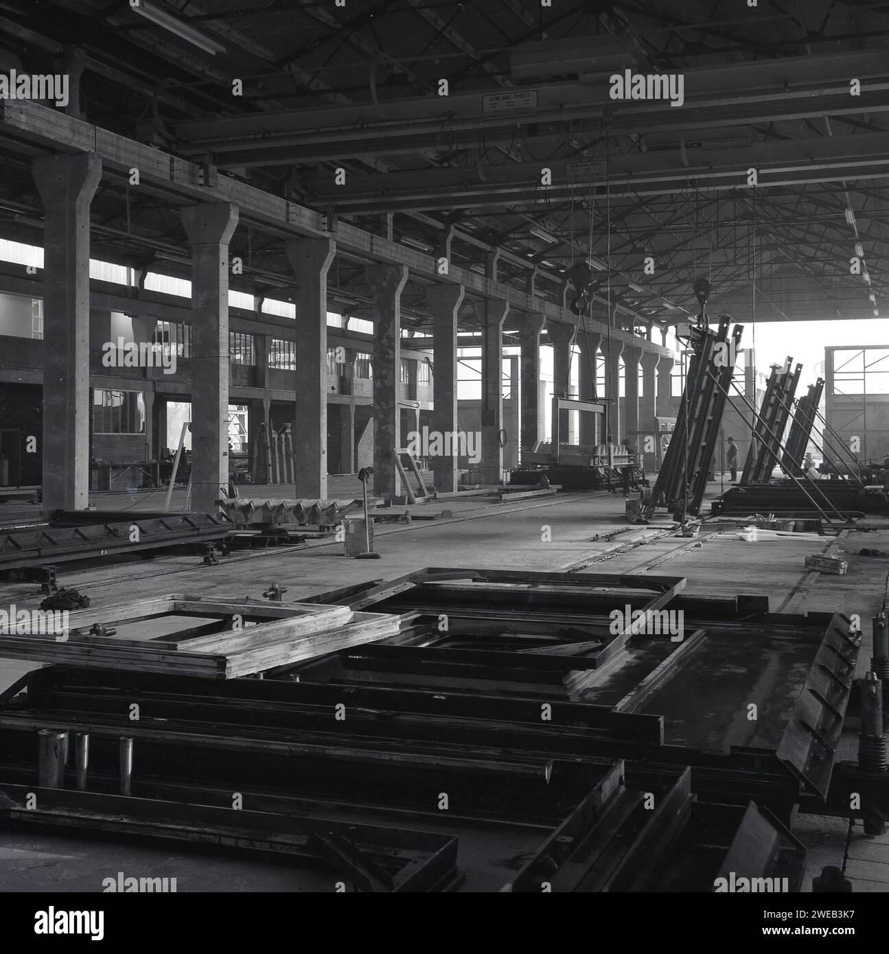 1960er Jahre, historisches Inneres eines großen „Hangar“-Gebäudes mit Grantry, in dem Fertigbetonplatten hergestellt werden, England, Großbritannien. Name oben auf der Gantry, Rowlan Priest, Cradley Heath, SWL 10 Tonnen. In Großbritannien in den späten 50er und 60er Jahren wurden große Turm- und Büroblöcke aus vorgegossenen Betonplatten errichtet, was eine schnellere und kostengünstigere Konstruktion und eine hervorragende Feuerbeständigkeit bedeutet. Stockfoto