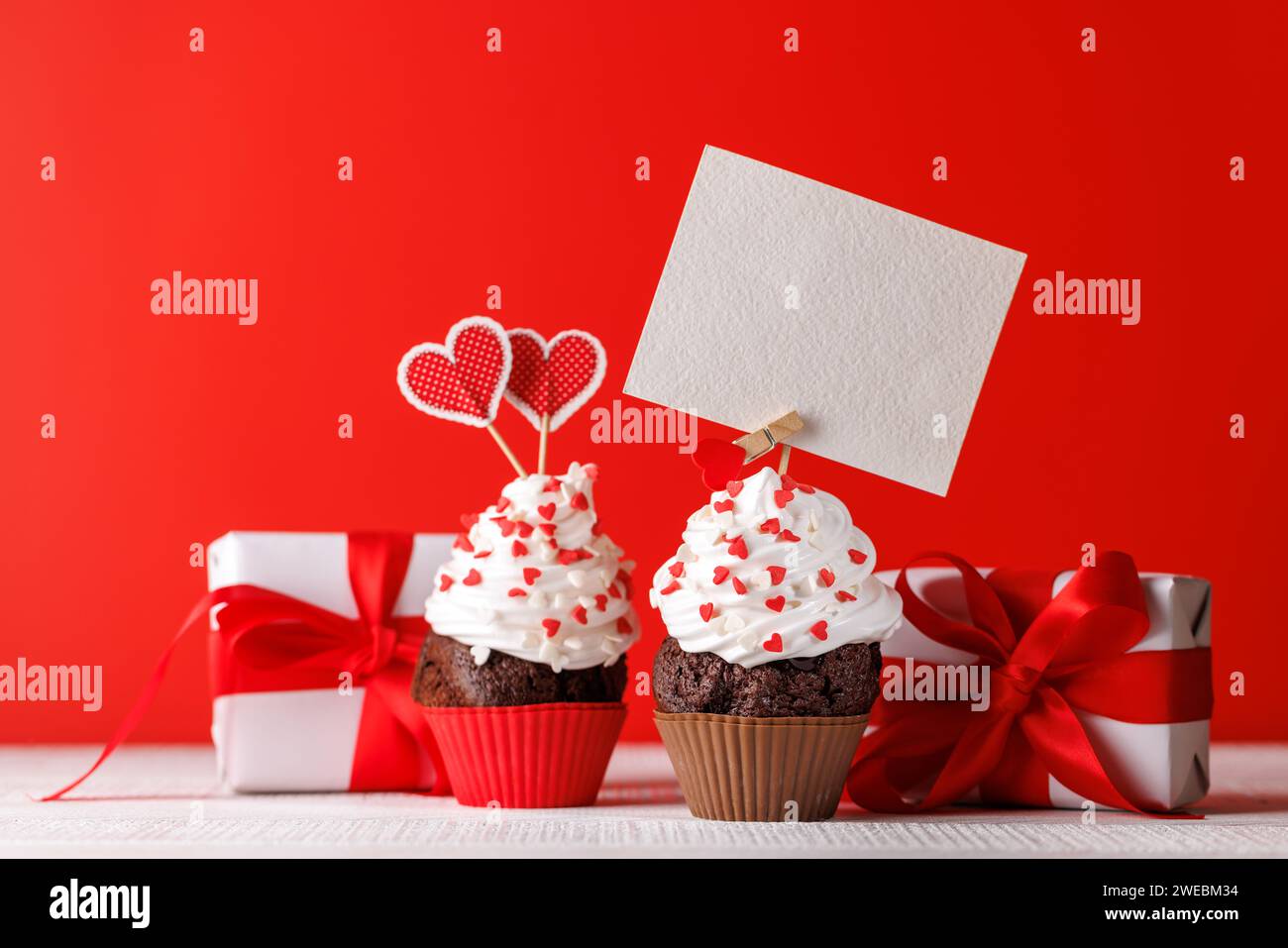 Cupcake Love: Herzhafte Leckereien vor leuchtendem rotem Hintergrund mit Kopierraum für Ihre Valentinstag-Grüße Stockfoto