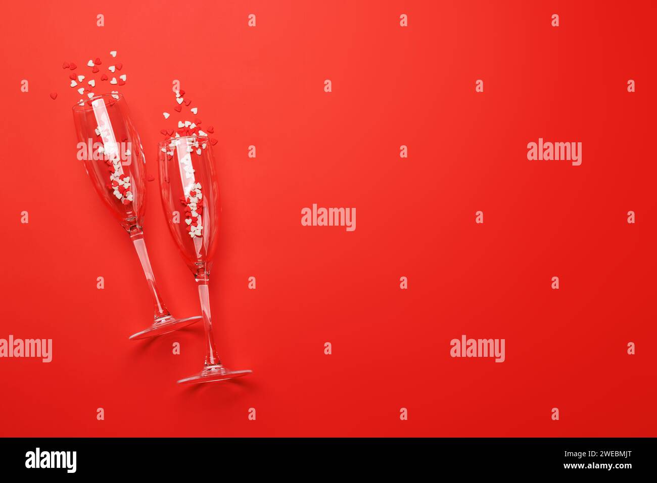 Sektgläser mit Herzbonbons auf rotem Hintergrund mit Textfeld. Grußkarte zum Valentinstag Stockfoto