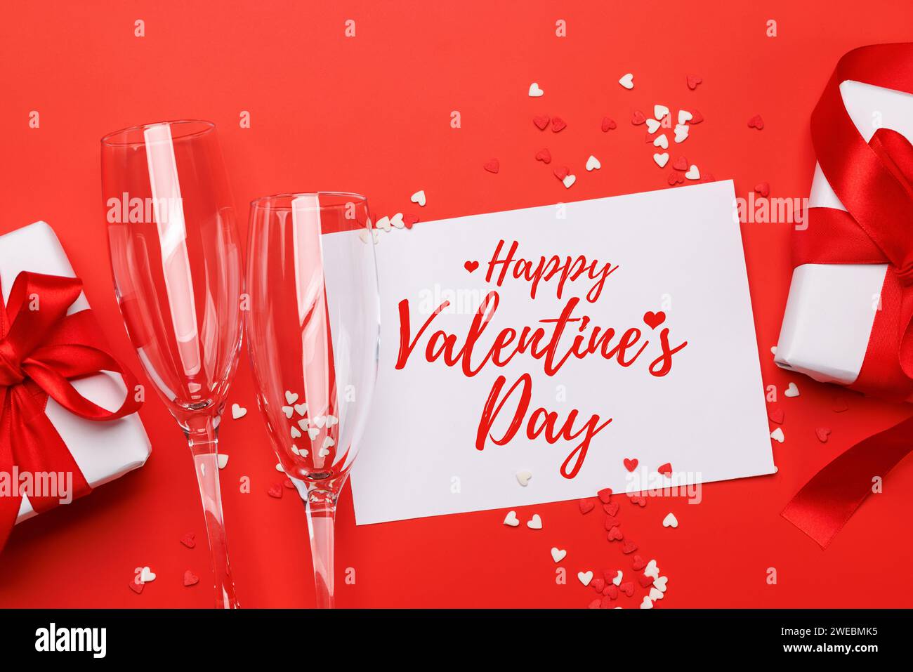 Champagner und Geschenk: Feierliches Duo auf rotem Hintergrund mit Textfeld. Grußkarte zum Valentinstag Stockfoto