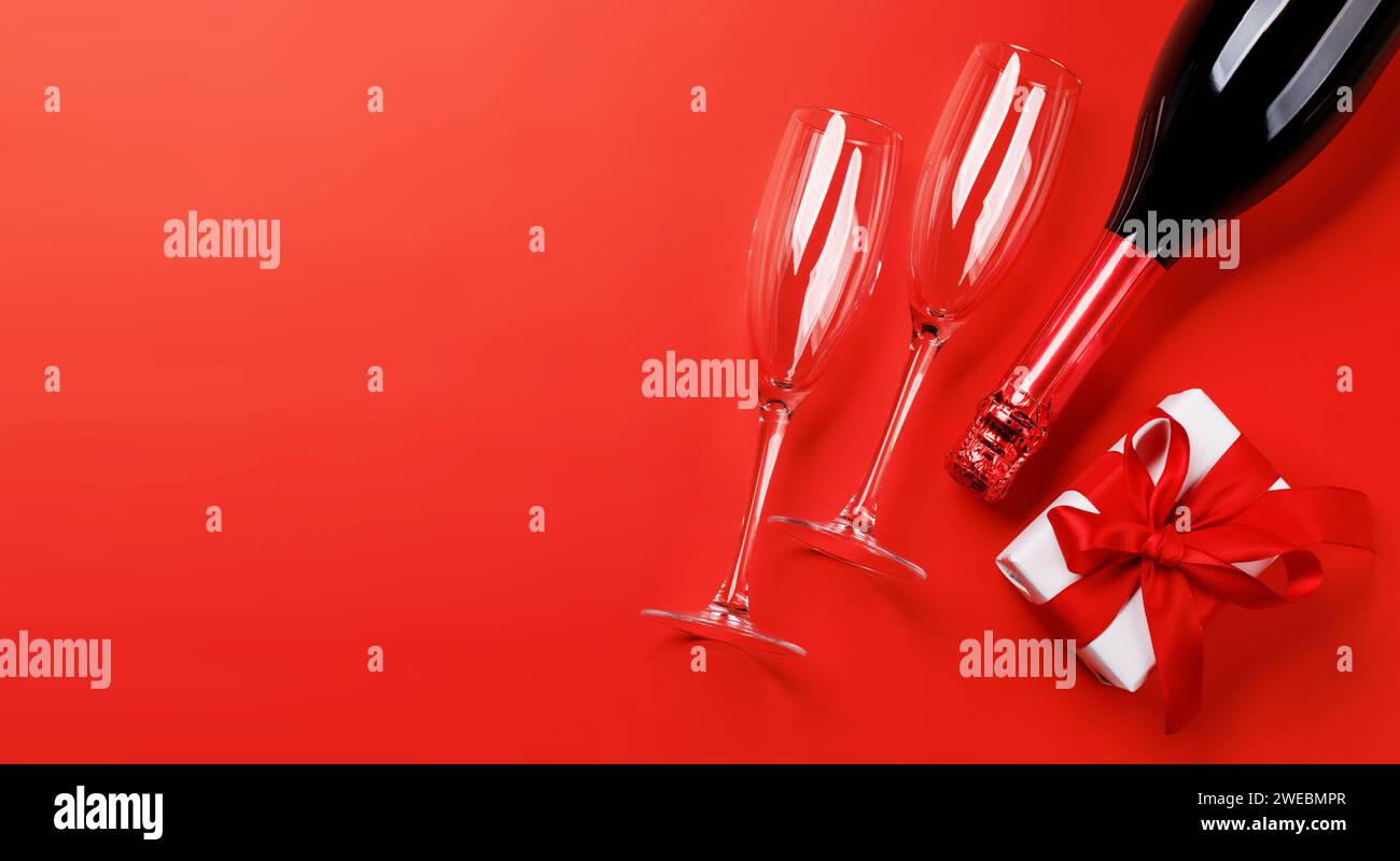 Champagner und Geschenk: Feierliches Duo auf rotem Hintergrund mit Textfeld. Grußkarte zum Valentinstag Stockfoto