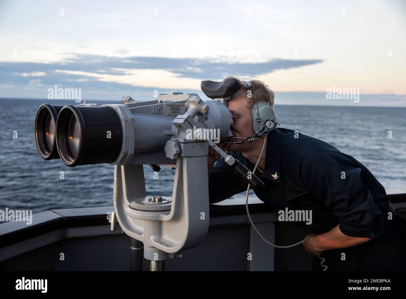 Cryptologic Technician (Collection) verwendet das Brückenflügelfernglas, um Kontakte nach vorne zu verfolgen, während ein See- und Ankerdetail an Bord des Arleigh Burke-Klasse-Raketenzerstörers USS Sterett (DDG 104) erfolgt. Stockfoto