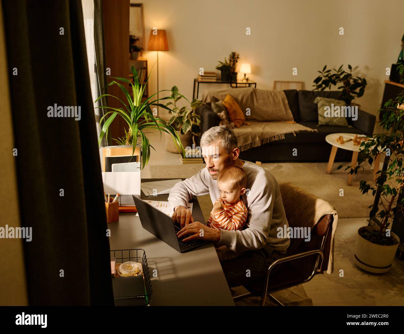Beschäftigter männlicher Solopreneur oder Manager und sein kleiner Sohn schauten auf den Laptop-Bildschirm, während er nach dem Frühstück am Tisch im Wohnzimmer saß Stockfoto