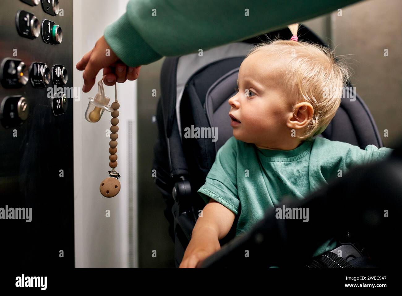 Ein kleines süßes Baby, das in einem Kinderwagen sitzt, drückt den Knopf am Boden im Fahrstuhl. Eine kleine Blondine in einer Kutsche fährt mit ihm den Aufzug hoch oder runter Stockfoto