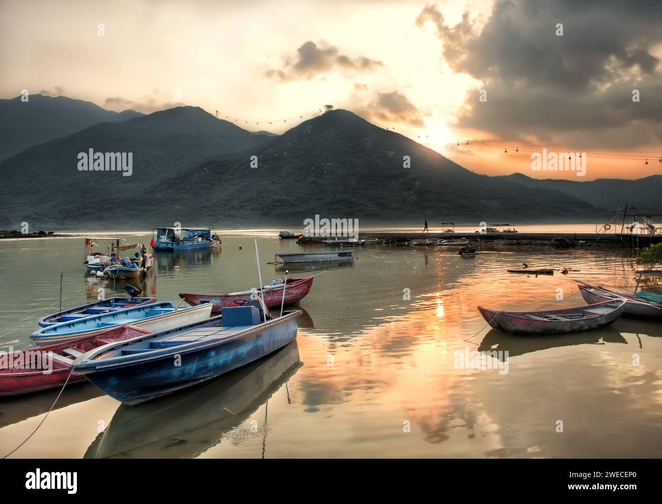 Sonnenuntergangsszene mit stillstehenden Fischerbooten mit Pier und Bergen in Tung Chung, Hongkong Stockfoto