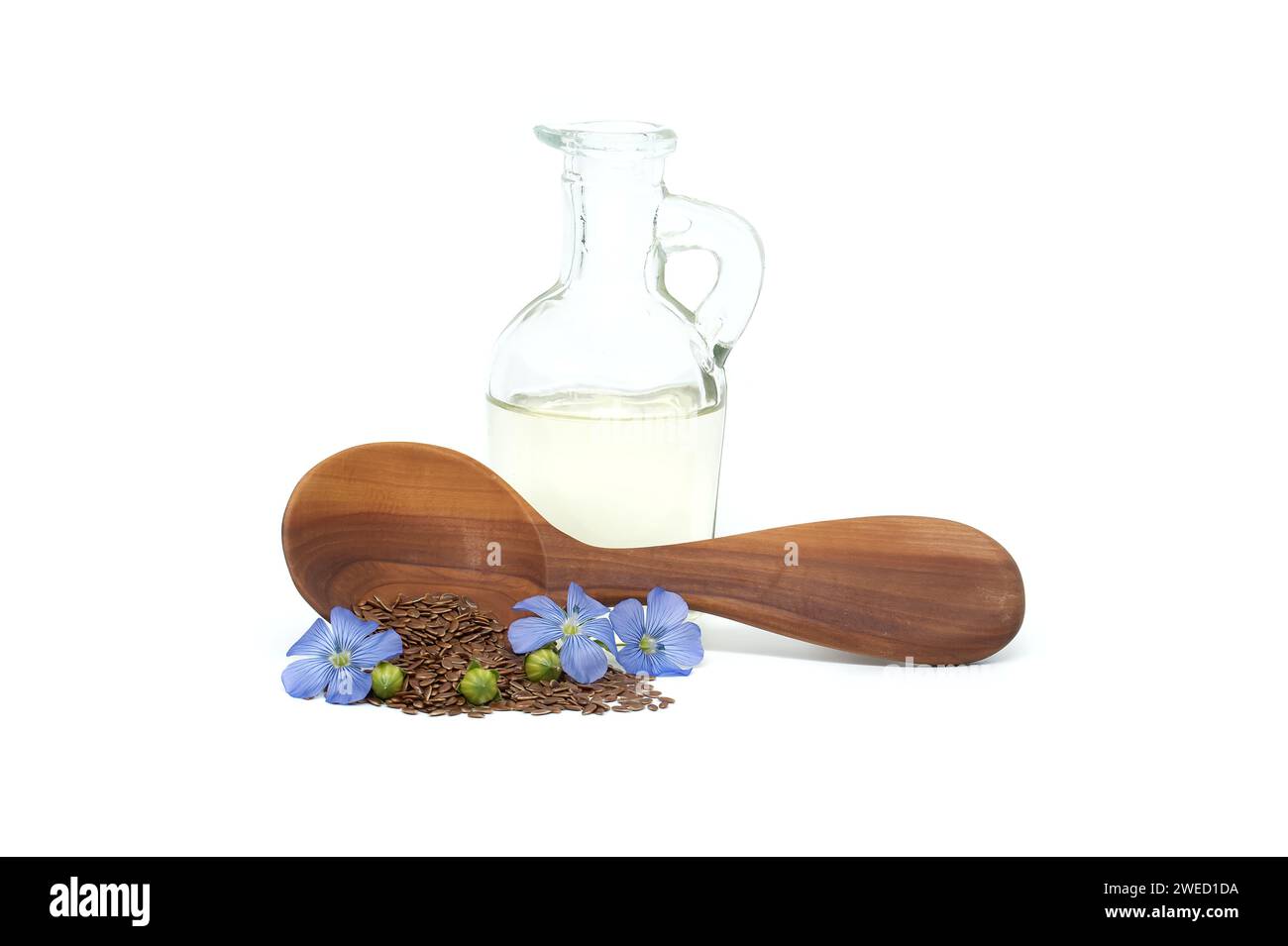 Holzlöffel gefüllt mit kleinen braunen Leinsamen und einer blauen Leinpflanze blüht neben Leinöl in Glasdekanter isoliert auf weißem Hintergrund Stockfoto