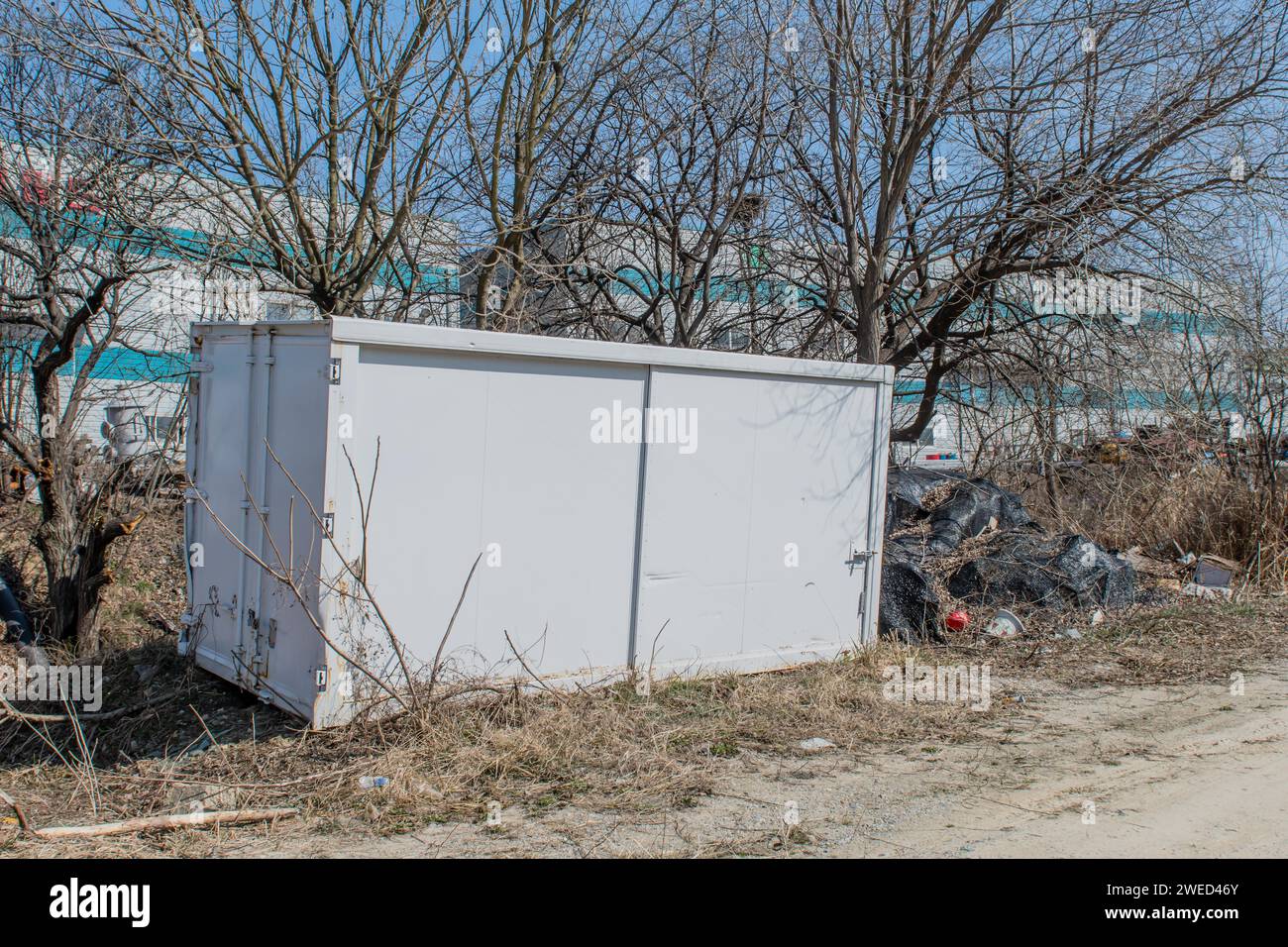 Lagercontainer aus weißem Metall, der vor Baumkronen im ländlichen Industriegebiet sitzt Stockfoto