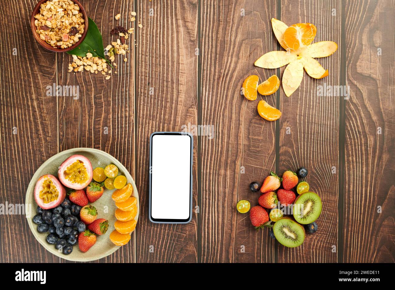 Smartphone mit leerem Bildschirm auf Holztisch mit Obst und Müslischale zum Frühstück Stockfoto
